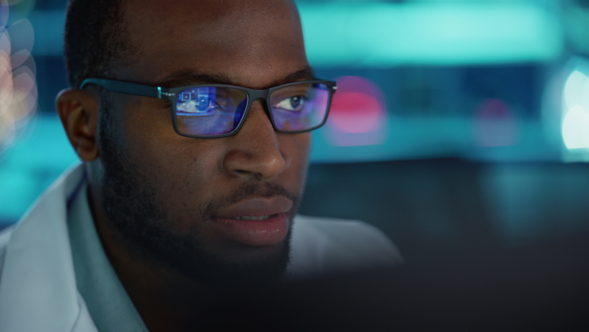 Portrait of Handsome Black Man Wearing Glasses Working Confidently on a Computer. Young Intelligent Male Engineer or Scientist Working in Laboratory. Bokeh Blue Background. Close-up Side View Shot Royalty-Free Stock Footage #1065341824