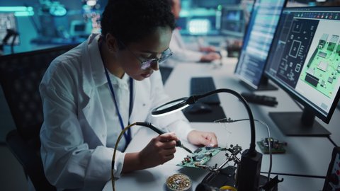 Modern Electronics Research, Development Facility: Black Female Engineer Does Computer Motherboard Soldering. Scientists Design Industrial PCB, Silicon Microchips, Semiconductors. High Angle Shot