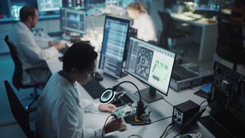 Modern Electronics Research, Development Facility: Black Female Engineer Does Computer Motherboard Soldering. Scientists Design Industrial PCB, Silicon Microchips, Semiconductors. High Angle View