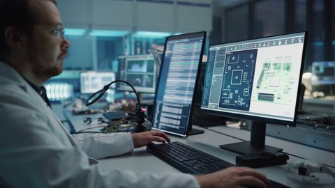 Modern Electronics Facility: Scientist, Engineer Works on Computer with CAD Software. Does Design, Development of Industrial PCB, Silicon Microchips, Semiconductors. Over the Shoulder Close-up