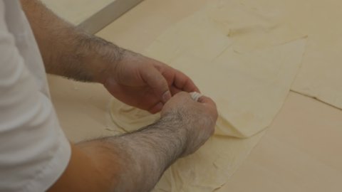 A male Asian baker uses his hands to separate thin layers of dough and place them in a baking tray to make Arabian baklava. Baking national desserts for Ramadan. top view