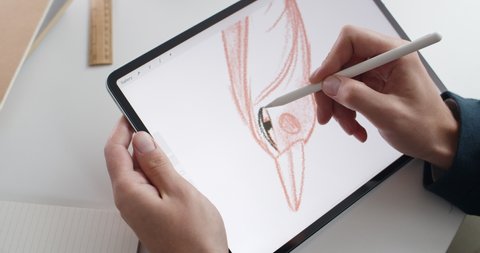 Lviv, Ukraine - May 28, 2020: Talanted graphic designer drawing bird on digital tablet computer. Focus on person hands creating illustration with stylus on notepad. Concept of modern art.