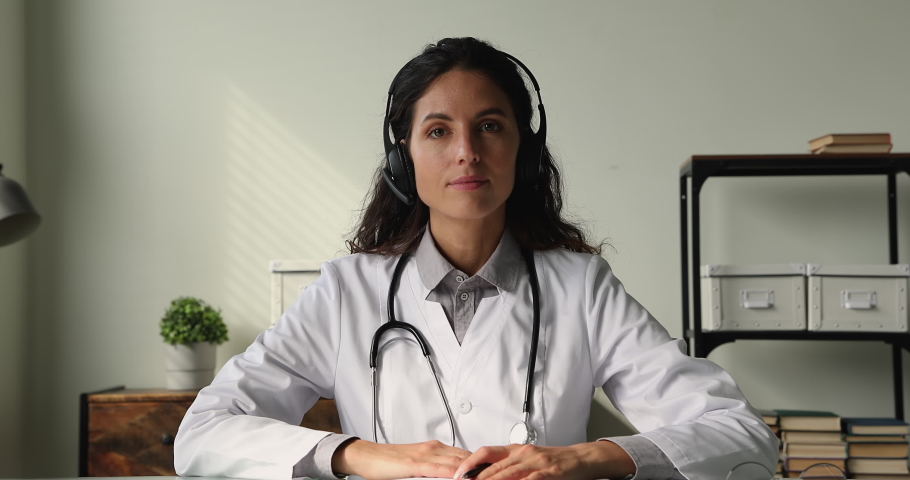 Female therapist in white coat sit at desk look at camera listens health complaints of client through headset provide professional aid by videocall. Telemedicine, healthcare services remotely concept Royalty-Free Stock Footage #1065349519