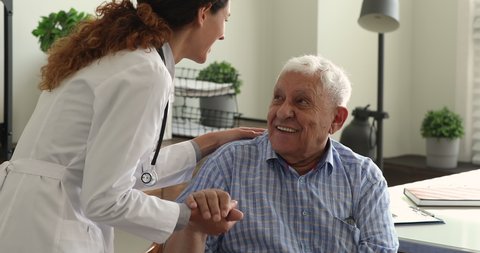 Young gp doctor holds senior male patient hand talk to him provide psychological support express kindness, give professional aid during visit in clinic. Elder care, medicare services for older concept