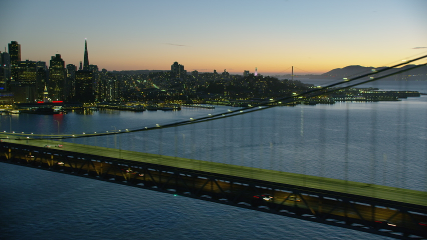 Aerial view San Francisco Oakland Bay Bridge illuminated at dusk downtown city skyscrapers quiet due to Coronavirus pandemic Lockdown California America