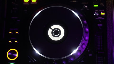 Rotating music record on a DJ console in a disco. Footage. Close-up of musical equipment for celebrations and parties. Beautiful neon lights and flashes of different colors