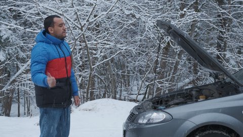 Man standing on road near broken car and trying to catch help on winter forest road