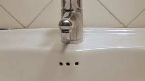 The faucet is opened, water flows into the drain basin, then was closed. Pouring water, crack in the tap