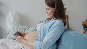Cheerful pregnant lady watching video of fetus moving in womb on smartphone screen smiling enjoying content. Pregnancy and modern technology concept.