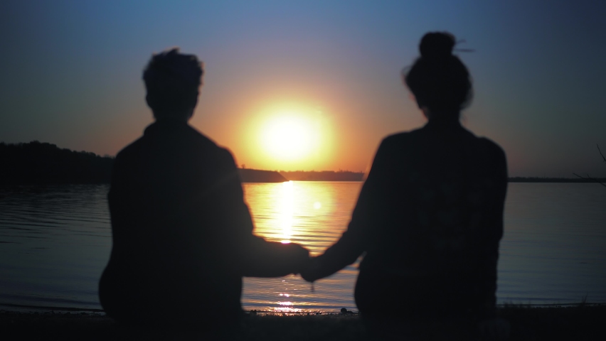 romantic couple hold hands on sunset, relaxing on beach, lookin at sundown