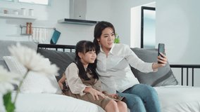 Asian family little kid girl and mother talking in video conference by smartphone together in living room at home with happiness and smile. Happy activity technology lifestyle mobile phone use concept