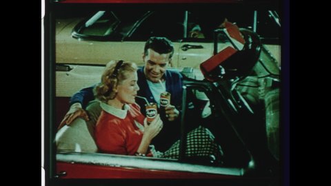 1950s USA Drive-in Movie Theater Intermission Announcement. Young Couple sit in Convertible Car at Drive-In Enjoying Refreshments: Drinks, Popcorn, and Hotdogs. 4K Overscan of Archival 16mm Film Print