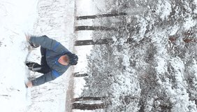 a young teenage man of Caucasian ethnicity in warm clothes throws up a pile of snow and smiles cutely. Active rest in the park in the winter season. Fun time concept, vertical video
