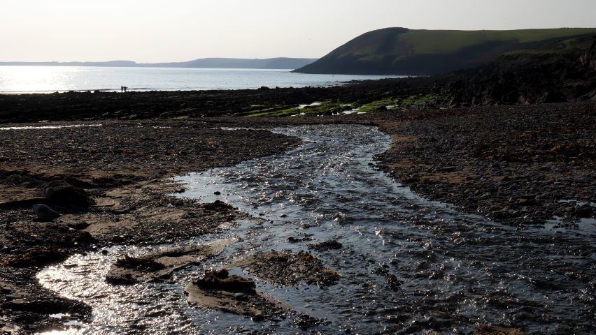 Low angle view of winding stream rushing into the sea before sunset.