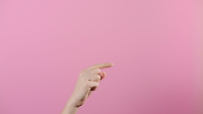 A woman's hand appeared from below and with her index finger shows the direction to the right. Pink background. The concept of gestures | Shutterstock HD Video #1065395461