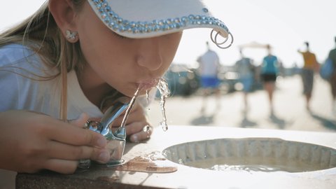 Girl having fun with drinking water fountain in Italy on warm and sunny summer day.