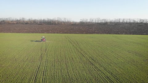 Tractor spreading artificial fertilizers in green field. Farmer fertilizing arable land with nitrogen and potassium fertilizer.