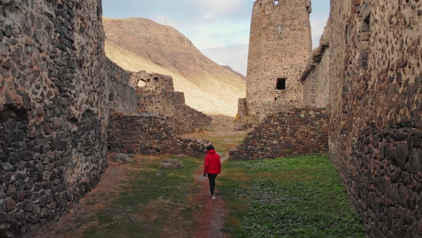 Female tourist walks down the path surrounded by Khertvisi fortress wall ruins. Cinematic filter and travel concept