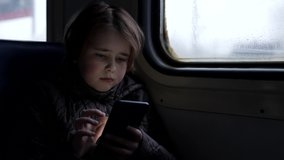 little girl is using smartphone, riding train, playing games in wagon, portrait