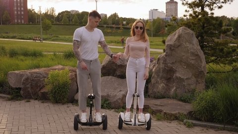 A young sports couple rides a gyro scooter in a beautiful Park in the summer at sunset. Happy man and woman riding on the hoverboard. Active lifestyle.