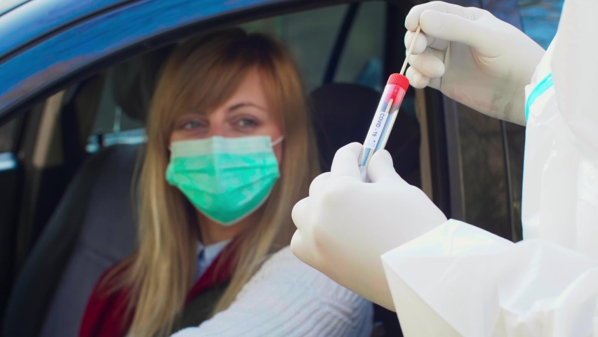 Medical worker performing drive-thru COVID-19 test, taking nasal swab sample from female patient through car window, PCR diagnostic for Coronavirus, doctor in PPE holding test kit. Royalty-Free Stock Footage #1065409453