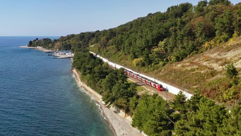 Sochi, Russia - 20 sep 2020: A passenger train rides along the seashore on a sunny day. Swallow. Russian Railways. Sochi, Russia. Electric train. Trip. Journey. Transport. Aerial video shooting.