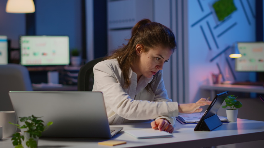 Manager woman using laptop and tablet in same time working overtime in business startup office. Busy multitasking employee using modern technology network wireless overworking writing, searching. | Shutterstock HD Video #1065410113