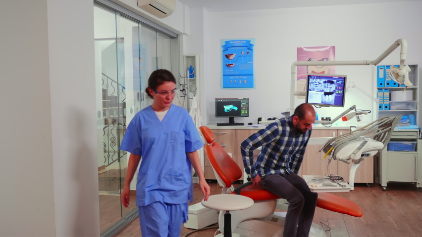 Nurse inviting next patient in stomatology room showing to lie on chair. Dentistry assistant sitting in modernconsultation dental room with man waiting for specialist dentist doctor. | Shutterstock HD Video #1065410782