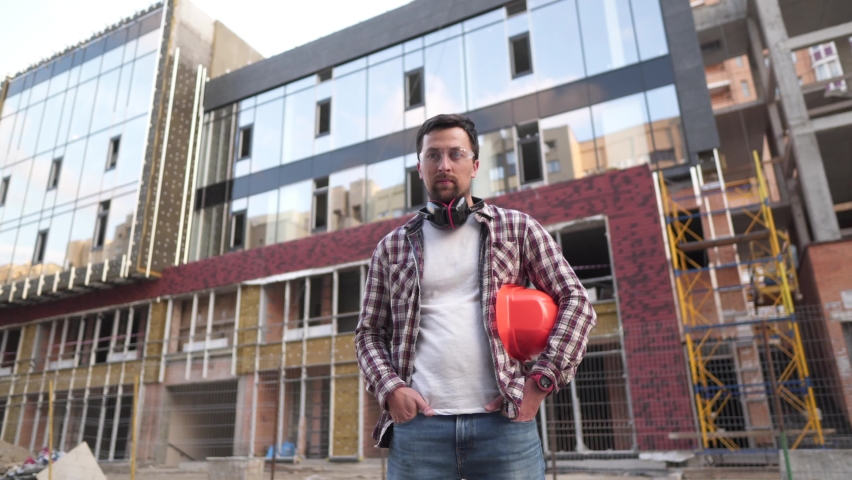 Happy proud craftsman. Portrait of construction engineer on building site and looking at camera. Handsome contractor in hardhat folding arms. Professions, construction, workers, architect concept | Shutterstock HD Video #1065417163