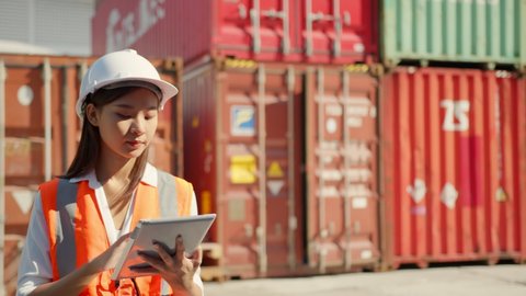 Asian engineer Foreman female worker working checking at Container cargo harbor holding tablet device to loading cargo containers. Dock female worker  Logistics import export shipping yard concept.
