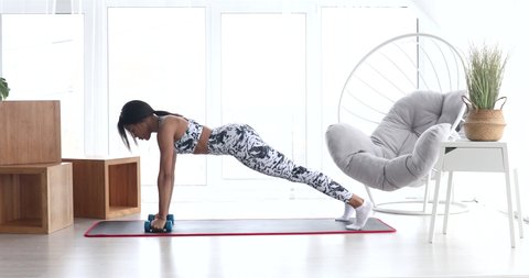 Athletic african american woman doing fitness at home with dumbbells.