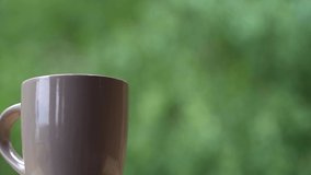 Closeup view video of cup with hot drink tea or coffee isolated on blurry green natural bokeh background
