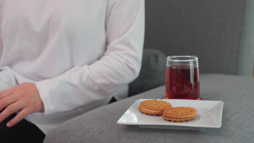 woman sitting on gray sofa drinking tea and eating biscuits