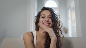 Portrait Of Young Woman With Long Curly Hair. She Is Sitting On The Couch. Amazing Look. Woman Smiles And Poses In Front Of The Camera. Woman Touches Her Chin With Her Hand. - Powered by Shutterstock - Get 15% off with code: PIKWIZARD15