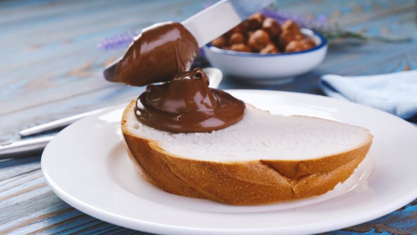 Spreading hazelnut cream on white bread slice, chocolate nut butter on school lunch toast Royalty-Free Stock Footage #1065427426