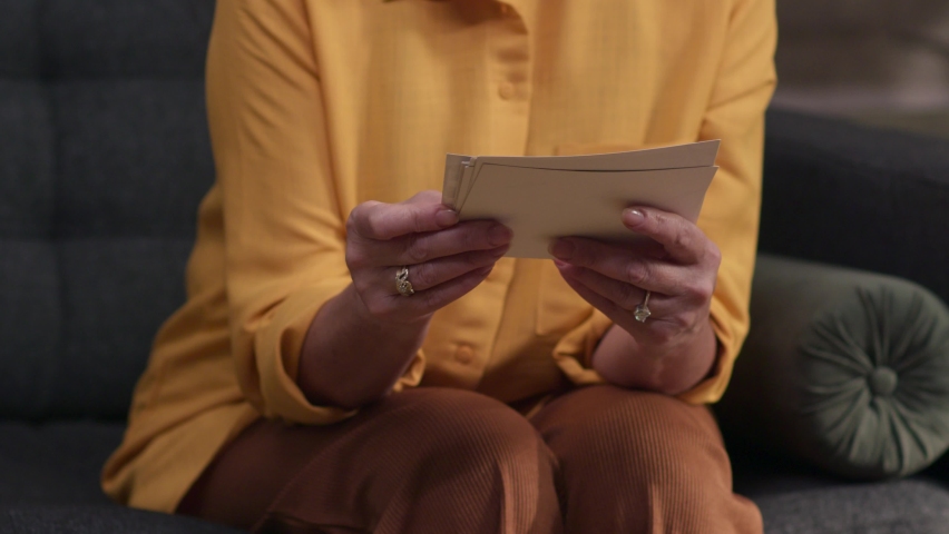 Close-up hands of woman looking at pictures on sofa. Memories concept.Slow motion.