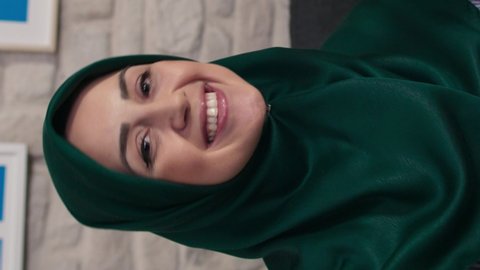 Happy woman in hijab is taking selfie while holding a mobile phone. Video for the vertical story.
