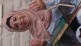 An old Muslim woman prays with a rosary after reading the Quran in her home. Islamic scripture, praying to the old person. Video for the vertical story.
