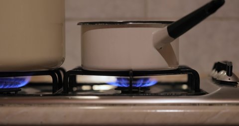 Cooking on gas stove, steam rising from saucepan, slider shot in dim kitchen
