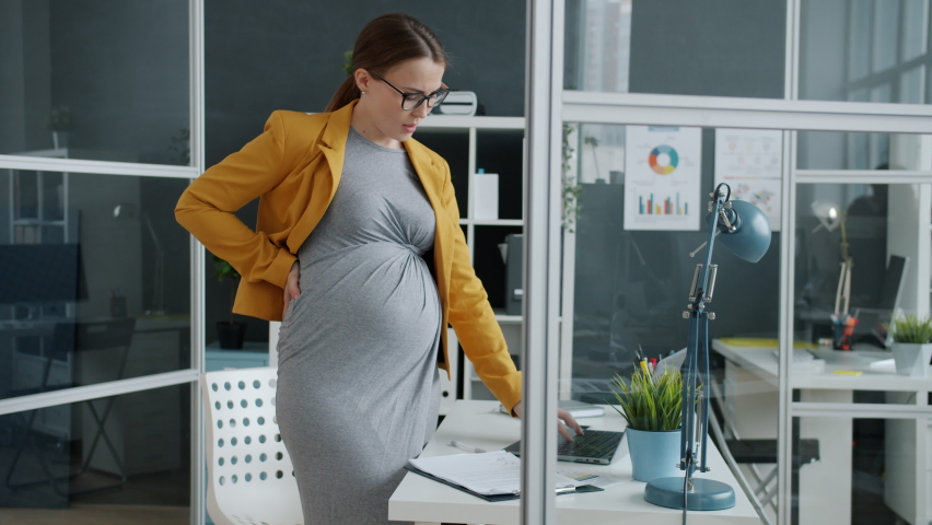 Pregnant young businesswoman is feeling stomach ache suffering from abdominal pain touching belly in workplace. People and healthcare concept. | Shutterstock HD Video #1065439120