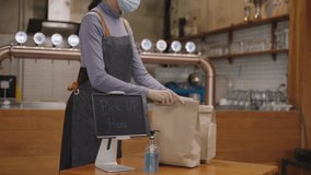 Young Asian restaurant owner or waitress wearing face mask, taking and preparing take away food bag to pick up point for waiting customer or courier to receive. Takeaway food during Covid-19 pandemic - Powered by Shutterstock - Get 15% off with code: PIKWIZARD15
