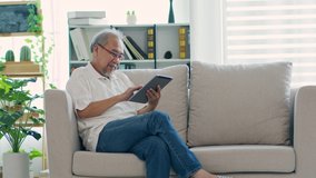 Happiness elderly asian man sitting on sofa using computer tablet and social media smile at home, Senior lifestyle at home concept