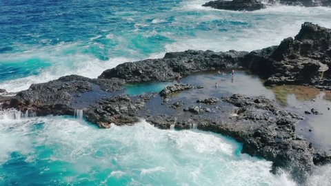 Travelers in wild nature, tourists enjoying ocean view. Adventure in wilderness, aerial 4K people swimming at tide pools. Stormy blue ocean waves crashing off volcanic shore. Men swimming in water