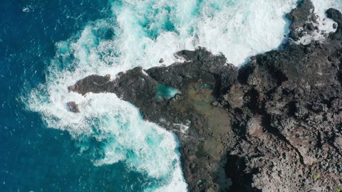Aerial 4K people relaxing at beautiful green pool on sunny day. Overhead view of men and women swimming in natural volcanic tide pools at stormy blue Pacific ocean on tropical Hawaii island shore USA