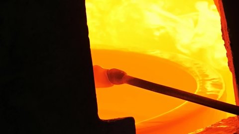 Traditional glass blowing process inhandmade glass studio. Glassblower keep the glassblowing pipe in gass furnace stove. Shining yellow flames.