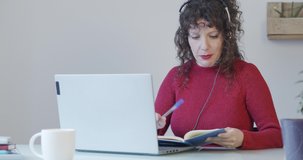 Woman working as a telemarketer with headphones in an office or from home writing in a notebook.Female receiving online classes