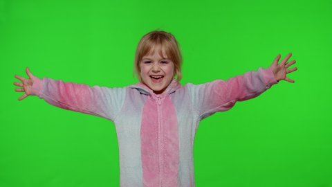 Young little blonde child 5-6 years old smiling, dancing, celebrating, making faces in unicorn costume on chroma key green background. Portrait of kid girl animator in unicorn pajamas. Slow motion