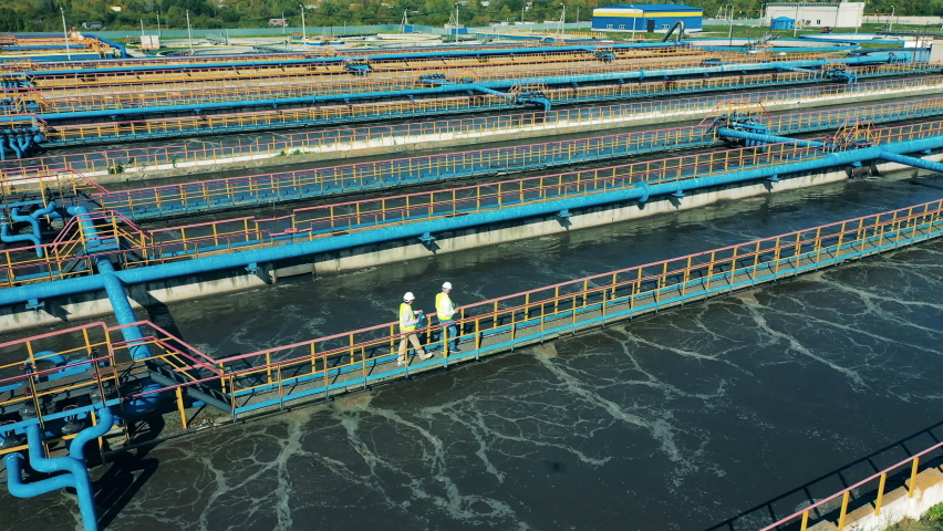 Drone shot of two specialists walking across the bridge at a water cleaning facility. Water management concept. Royalty-Free Stock Footage #1065463132
