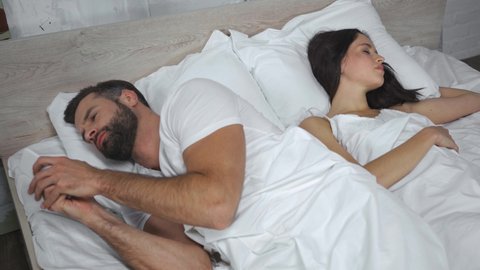 bearded man texting on smartphone while looking and sleeping wife