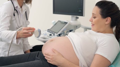 Attractive pregnant woman having ultrasound screening by professional gynecologist at medical clinic. Concept of people and health care.